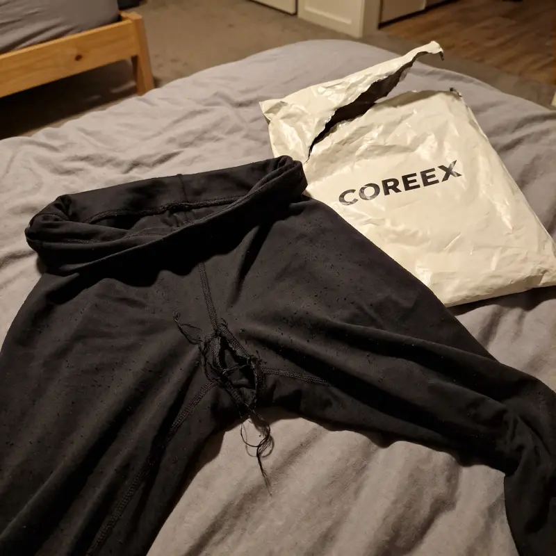 COREEX Leggings mit aufgegangener Naht neben der Versandtüte auf dem Bett
